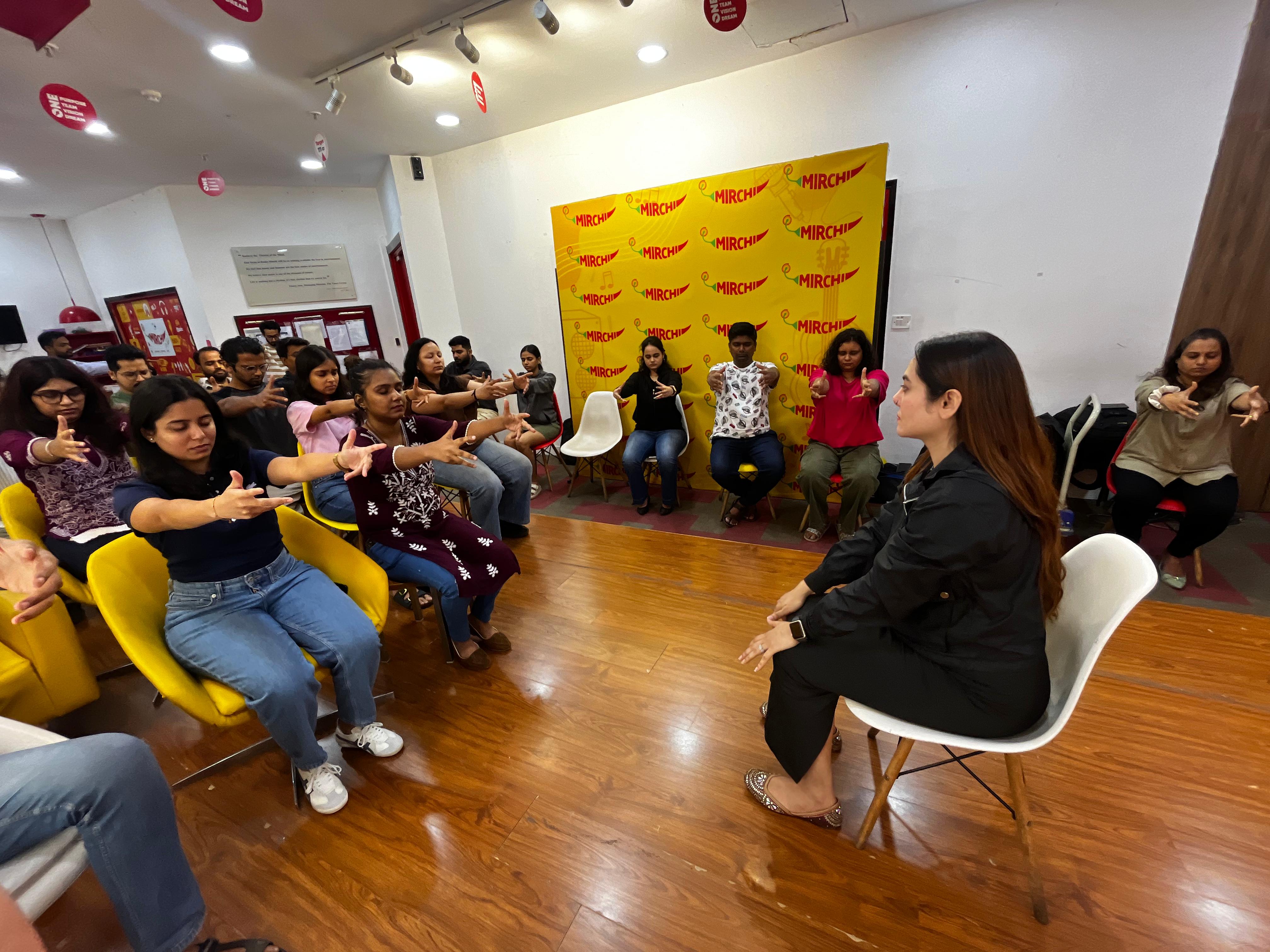 A wide view of a workshop room with participants seated in a semicircle following an exercise led by Vibha Jain.