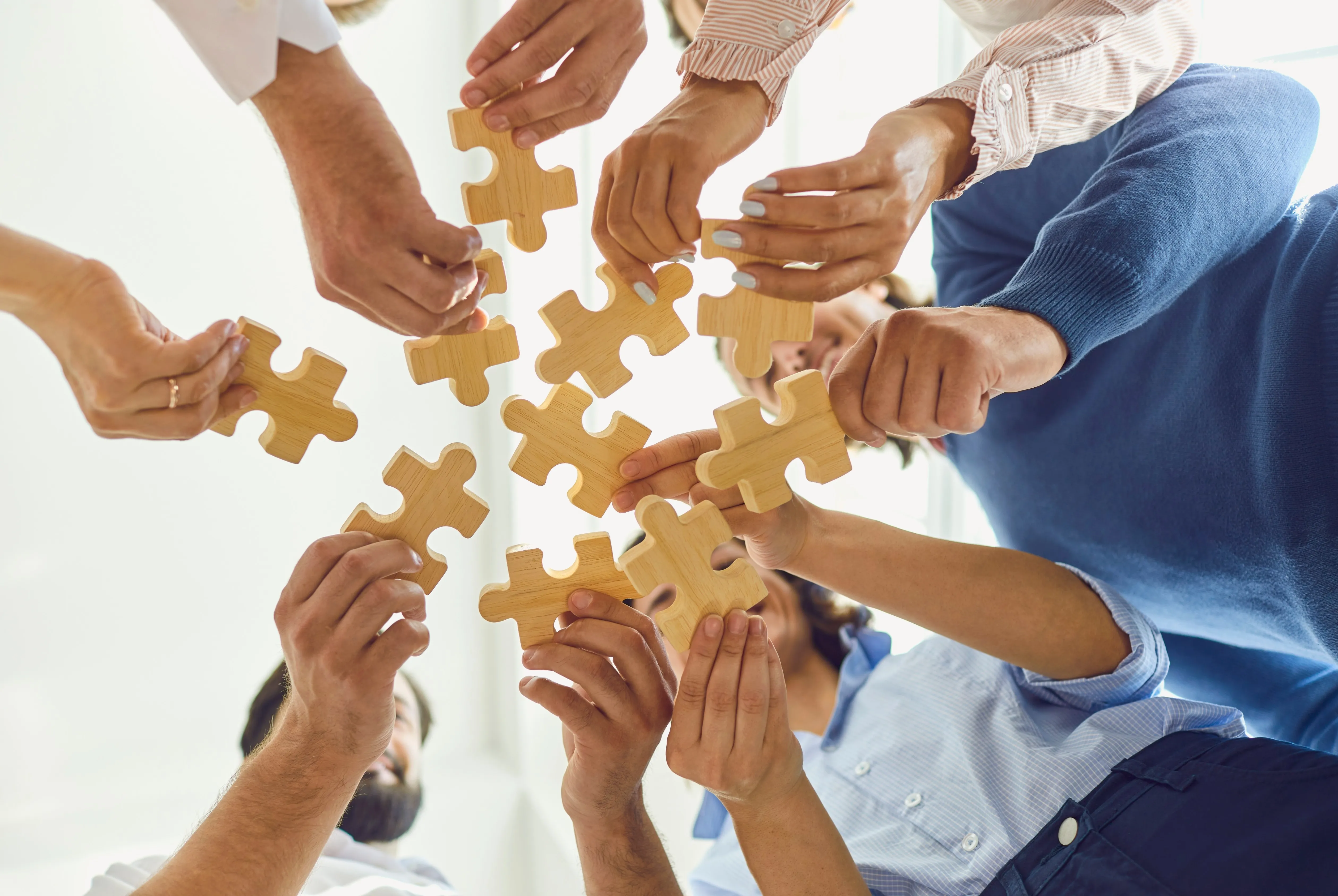 Several people standing in a circle, each holding a wooden puzzle piece and fitting them together.