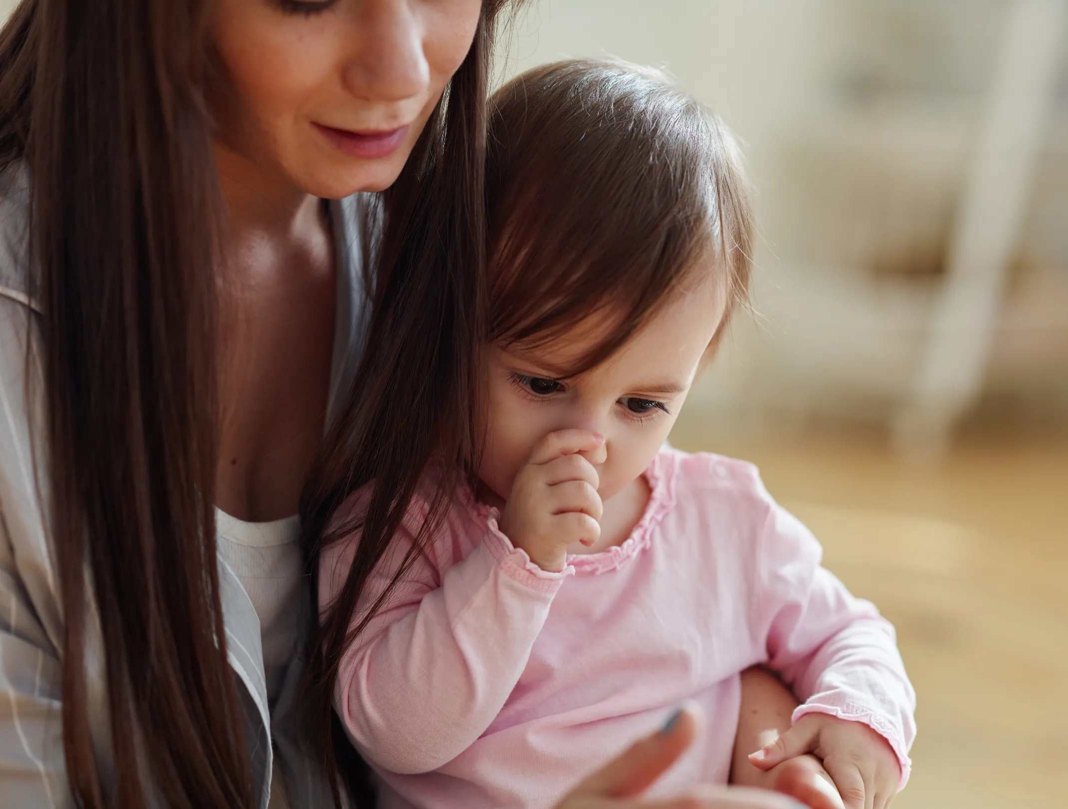 A parent holding a young child who is quietly sucking a thumb while they look at something together.