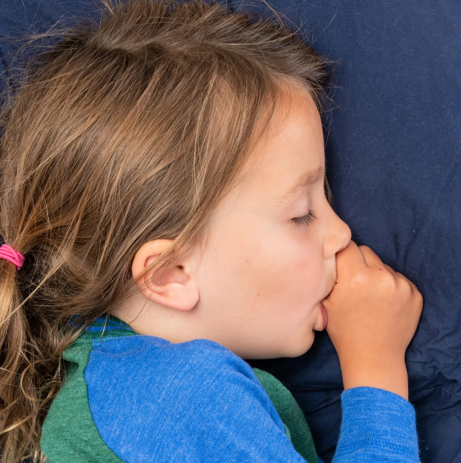 A child sleeping peacefully on a pillow with a thumb resting at the mouth.